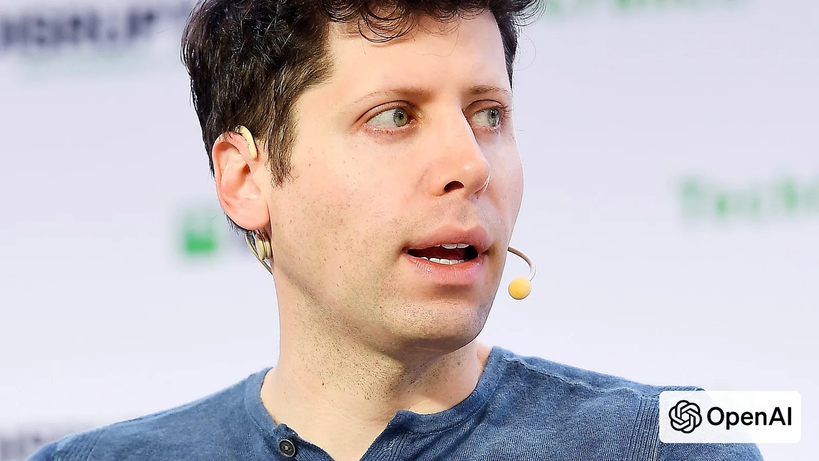 OpenAI CEO Sam Altman speaking at TechCrunch, with the OpenAI logo